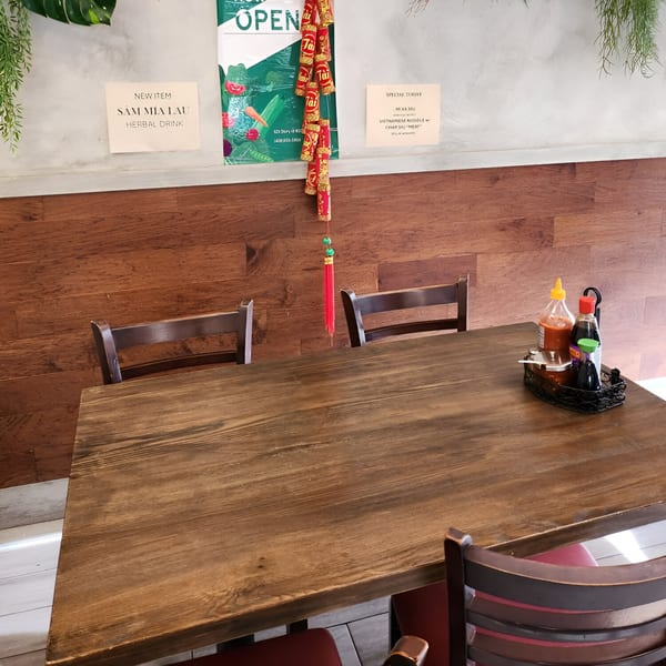 Empty wooden dining table with chairs, condiments, and Vietnamese restaurant signs on the wall.