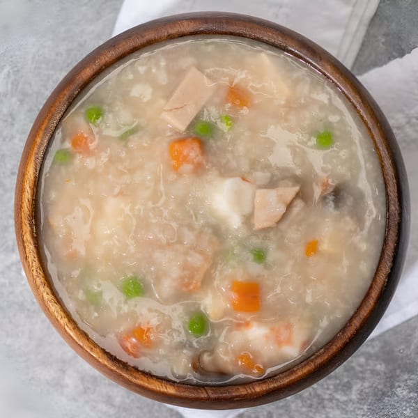 Overhead view of a wooden bowl filled with Vietnamese congee, featuring chicken, peas, and carrots.