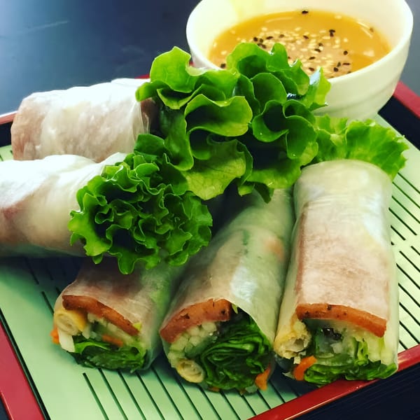 Fresh Vietnamese spring rolls with lettuce, vegetables, and meat, served with a sesame dipping sauce.