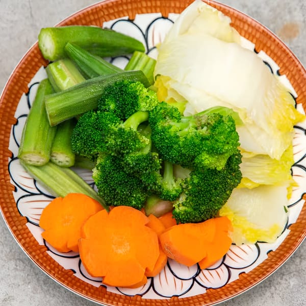 A colorful plate of steamed vegetables including okra, broccoli, napa cabbage, and carved carrots.