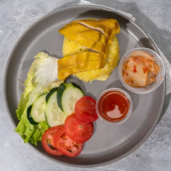 Vietnamese chicken rice with sliced chicken, yellow rice, fresh salad, chili sauce, and kimchi.