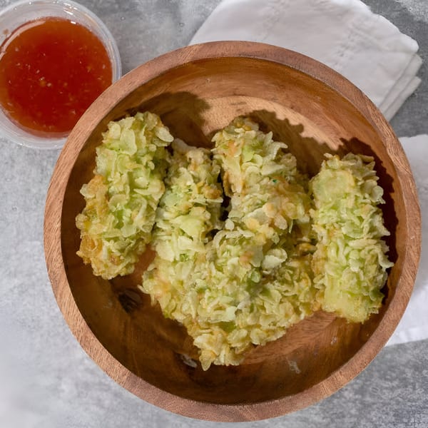 Crispy green fried banana fritters in a wooden bowl with a side of sweet chili sauce.