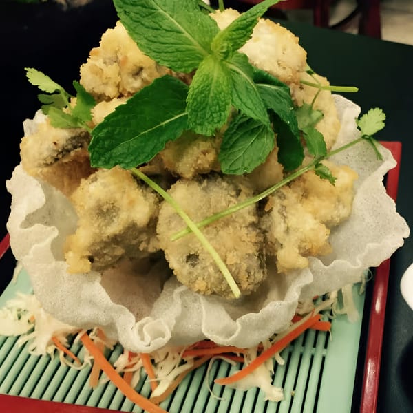 Crispy fried Vietnamese dish, garnished with fresh mint and cilantro, served on a bed of shredded vegetables.