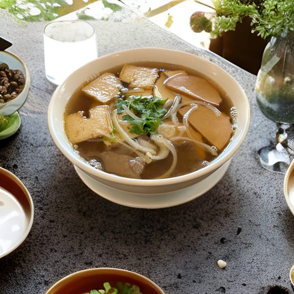 A bowl of Vietnamese pho with tofu, noodles, and cilantro on a dark table.