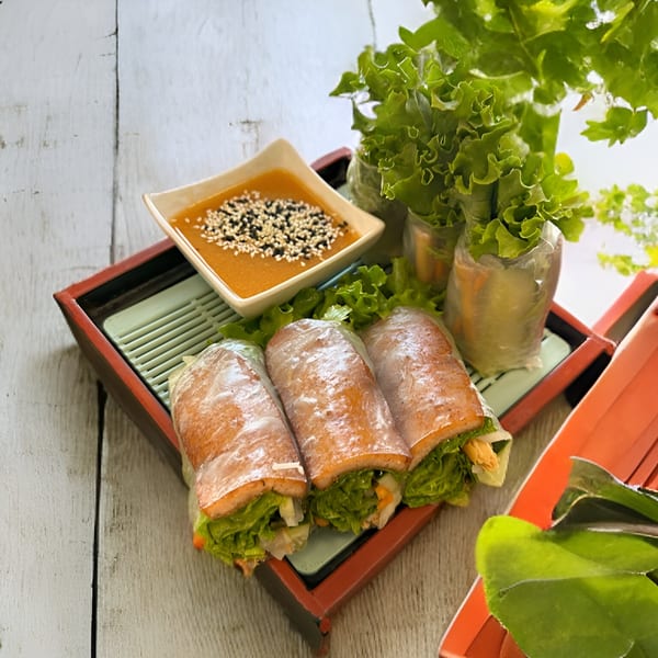 Vietnamese spring rolls with fresh lettuce and a sesame seed dipping sauce on a wooden tray.