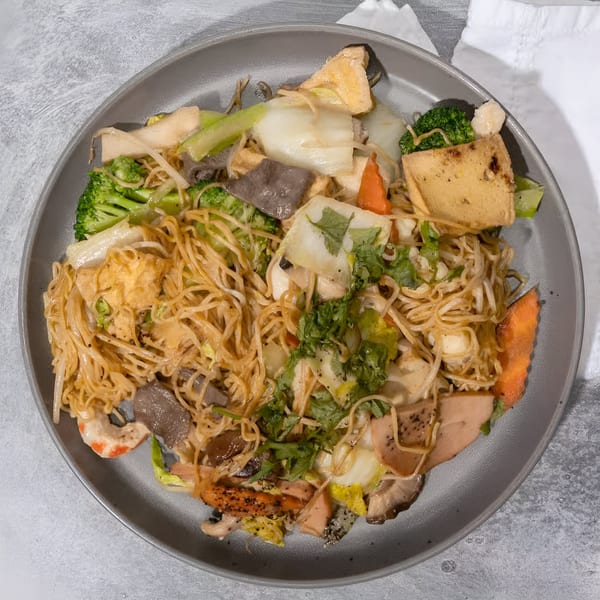 Vietnamese stir-fried noodles with broccoli, tofu, carrots, mushrooms, and cilantro on a gray plate.