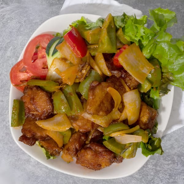 Vietnamese stir-fried chicken with green and red bell peppers, onions, and lettuce on a white plate.